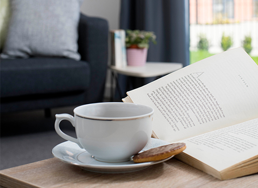 Photo showing a cup and saucer with a biscuit on a table next to an open book